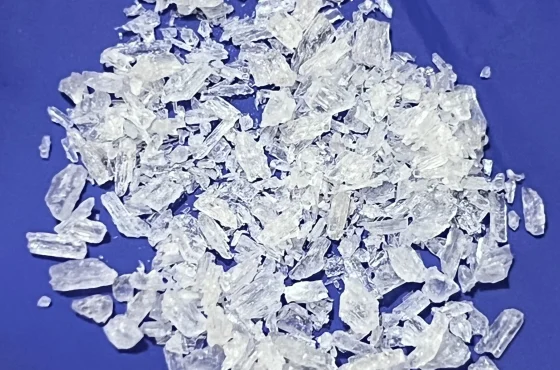 A heap of clear methamphetamine crystal shards of mixed size on a deep blue cloth background