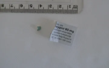 Oxycodone tablet fragment beside an Oxypro 80 mg prolonged-release package label